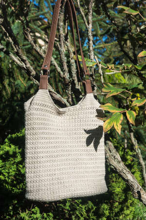 Cream crocheted handbag behind the bush in the garden in late summer on countrysideの写真素材