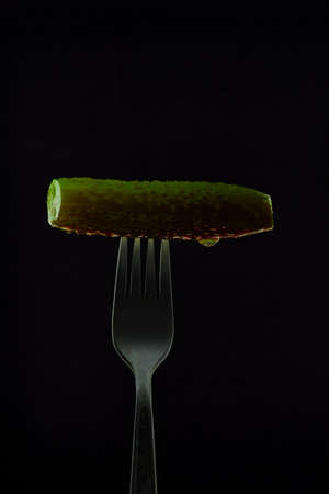 Juicy, salty, green cucumber on a fork, on a dark backgroundの写真素材