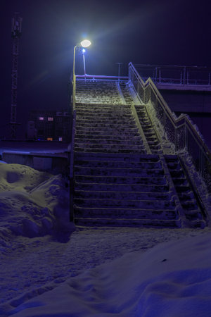 Snow-covered stairs to the pedestrian bridge at night in the light of lanterns.の写真素材