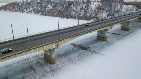 Car bridge over frozen river aerial drone view. Winter transport theme.