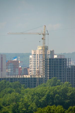 Construction of a high-rise building on a background of green treesの写真素材