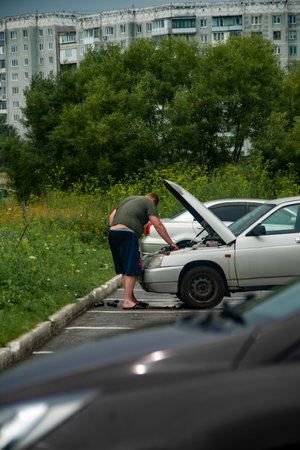 A man with a broken car stands on the road near the car