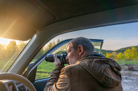 A man in a car with a camera in his hand looks through the window