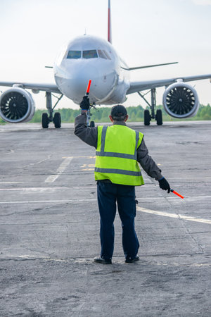 Ground Crew in the signal vest. Aviation Marshall / Supervisor meets passenger airplane at the airport. Aircraft is taxiing to the parking place.の写真素材