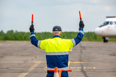 Rear view A signalman meets a passenger plane at the airport in front of a propeller airplane. The...