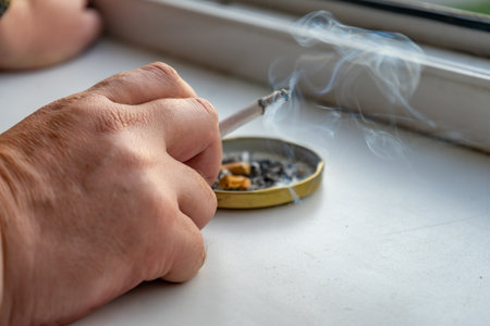A hand with a cigarette of a man smoking by the windowの写真素材