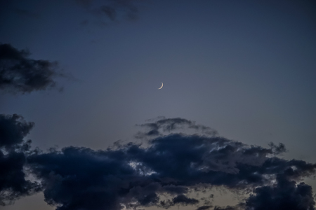 A thin Crescent moon in the night sky on the background of cloudsの写真素材