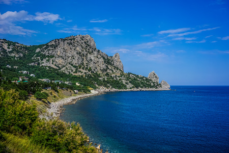Rock covered with green vegetation hanging over the calm blue sea in a bright summer dayの写真素材