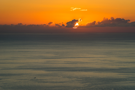 Seascape with sunset and the sun behind the dark clouds on a blue sea backgroundの写真素材