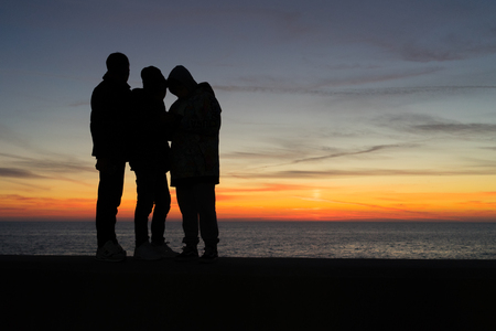 The dark silhouettes of the children against the background of sea and sky at sunset in winter. Sochi. Russia.の写真素材
