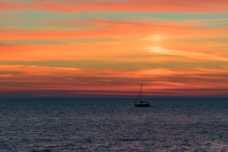Seascape with a vibrant sunset over a calm sea and a floating boat.の写真素材