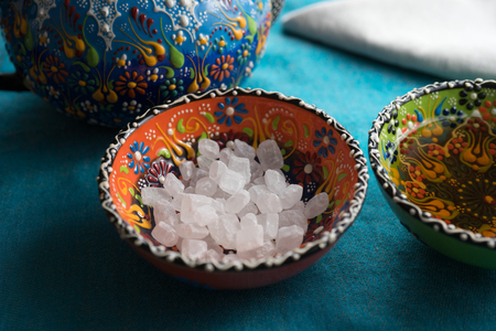 Large crystals of white sugar in colorful patterned ceramic bowl in turquoise textile tablecloths.の写真素材