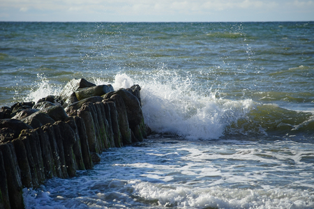 Wave with small white spray crashing against the coastal breakwater at the Baltic sea.の写真素材