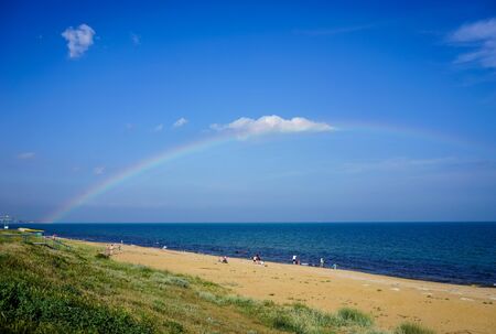 Feodosia, Crimea-June 16, 2016: Seascape with beautiful multicolored rainbow over the sea and sandy beach with resting people.のeditorial素材