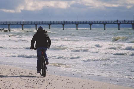 Zelenogradsk, Russia-may 17, 2016: A lone cyclist in dark clothes rides on a sandy beach towards the pier.の写真素材