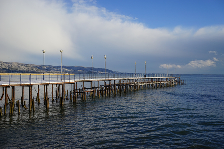 Seascape with old destroyed pier on the background of snow-capped hills and cloudy sky.の写真素材