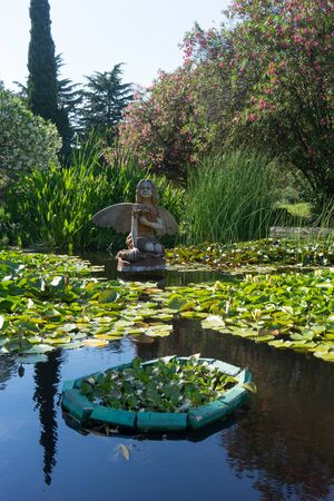 Sochi, Russia-June 24, 2018: landscape with a wooden statue of a fairy in a small pond with water liliesのeditorial素材
