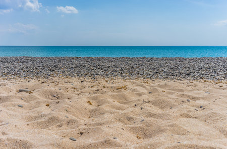 Sunny beach on the sea with sand and pebbles under the blue skyの写真素材