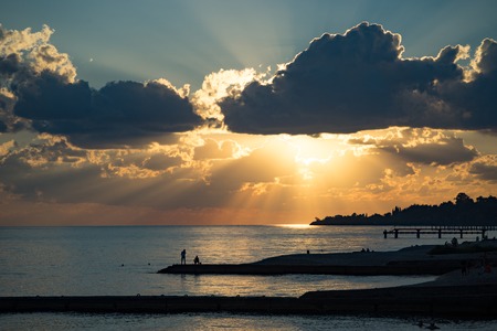 Coastline with beaches, breakwaters and people silhouette against a bright sunset and dramatic sky.の写真素材