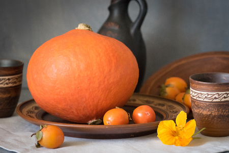 Autumn still life with a large pumpkin and persimmon in ceramic dishes.の写真素材