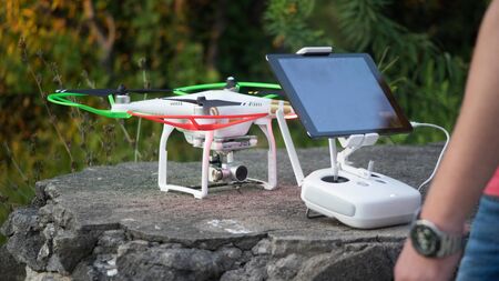 A man sets up a quadcopter and a remote with a tablet for flying.のeditorial素材