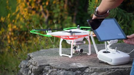 A man sets up a quadcopter and a remote with a tablet for flying.のeditorial素材