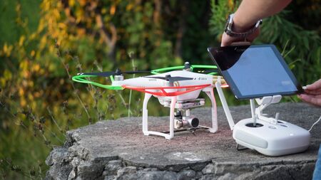A man sets up a quadcopter and a remote with a tablet for flying.のeditorial素材