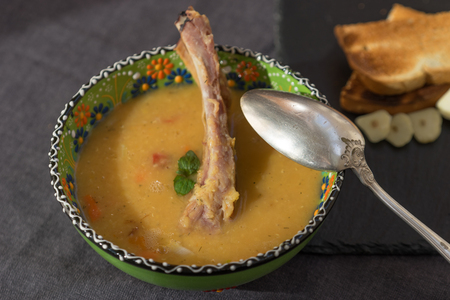 red lentil soup with smoked ribs in a light green bowl with floral ornament. Dark grey fabric background.の写真素材
