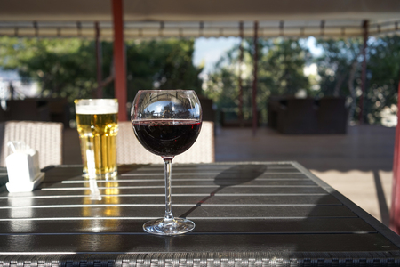 A glass of red wine on the table in a summer cafe on a blurred background with a glass of beerの写真素材