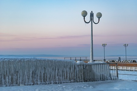 Winter landscape with icy fence on the background of the sky and the sea.の写真素材