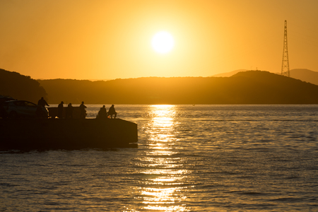Vladivostok, Russia-September 16, 2018: Seascape fishermen catch fish from the pier against the orange sunset.の写真素材