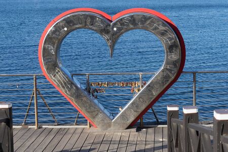 urban landscape with a metal heart on the background of the sea.のeditorial素材