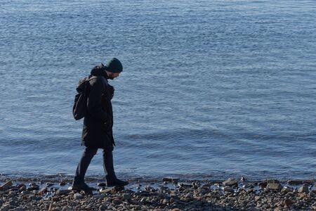 Young man in winter coat on blue sea backgroundのeditorial素材