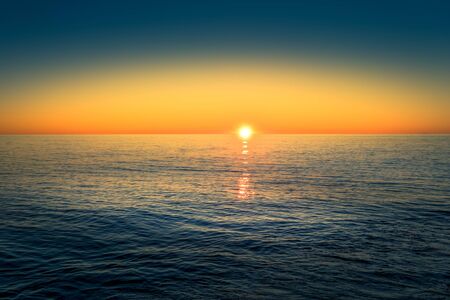 Seascape with a beautiful sunset over the horizon and the water surface.の写真素材