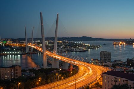 Cityscape overlooking the Golden bridge in blue hour. Bright illumination adorns the night city. Vladivostok, Russiaの写真素材