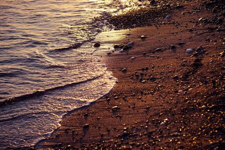 Background with water surface and sandy beach reflecting sunset light.の写真素材