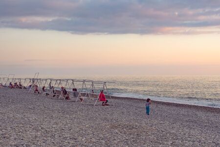 Sunset over the pebble beach. People sit in deck chairs and a swing and enjoy nature.のeditorial素材