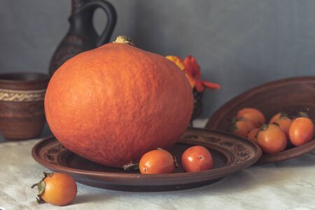 Autumn still life with pumpkin and nasturtium flowers. On the table there is a ceramic tableware and a tablecloth made of natural materials.の写真素材