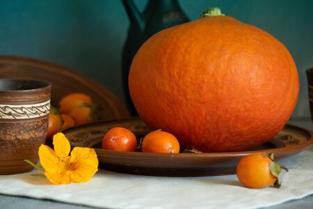 Autumn still life with pumpkin and nasturtium flowers. On the table there is a ceramic tableware and a tablecloth made of natural materials.の写真素材