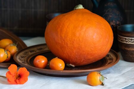 Autumn still life with pumpkin and nasturtium flowers. On the table there is a ceramic tableware and a tablecloth made of natural materials.の写真素材