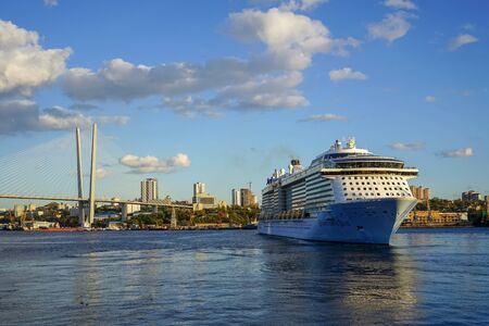 Vladivostok, Primorsky Krai-September 18, 2019: seascape with a beautiful cruise ship on the background of the city. In the background, the landmark Golden bridge.のeditorial素材
