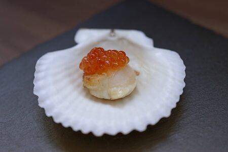 Red caviar on a scallop fillet and on a white shell on a dark slate background.の写真素材