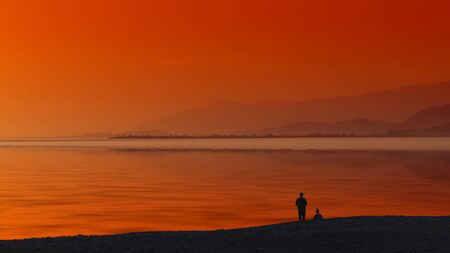 Seascape with orange sunset and silhouettes of people on the beach.の写真素材