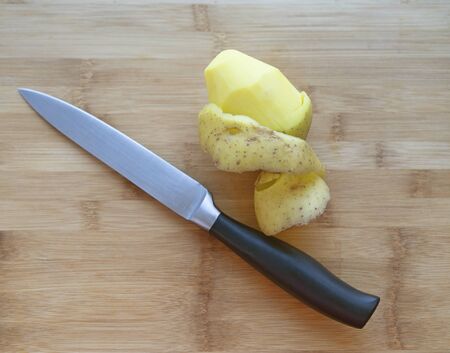 Peeled potatoes and a sharp knife on the background of a wooden surfaceの写真素材