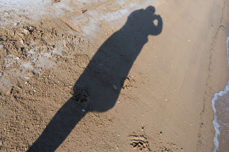 Background with the shadow of a man on the sand. Silhouette of a woman photographer.の写真素材