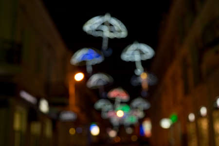 Blurred background of the city at night with bright glowing silhouettes of umbrellasの写真素材