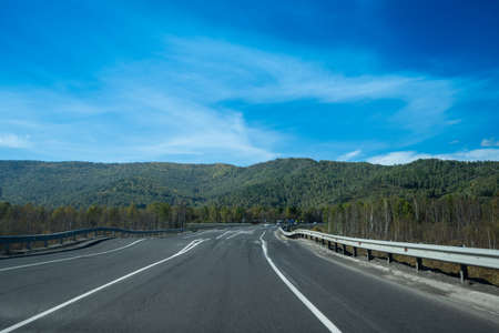 A landscape with a winding highway under a cloudy sky. Irkutsk region, Russiaの写真素材