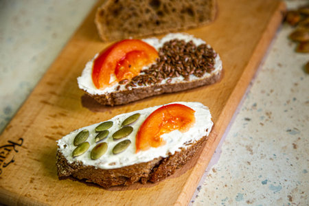 fast cooking food at home, eco bread with cream cheese, tomato slices, pumpkin and flax seeds, close...