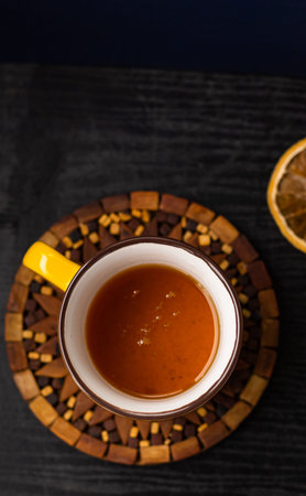 Top view  hot herbal tea in a yellow cup on a black wooden textured table, dried orange slice, brown...