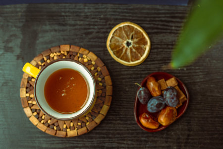 Top view  hot herbal tea in a yellow cup on a black wooden textured table, dried orange slice, brown...